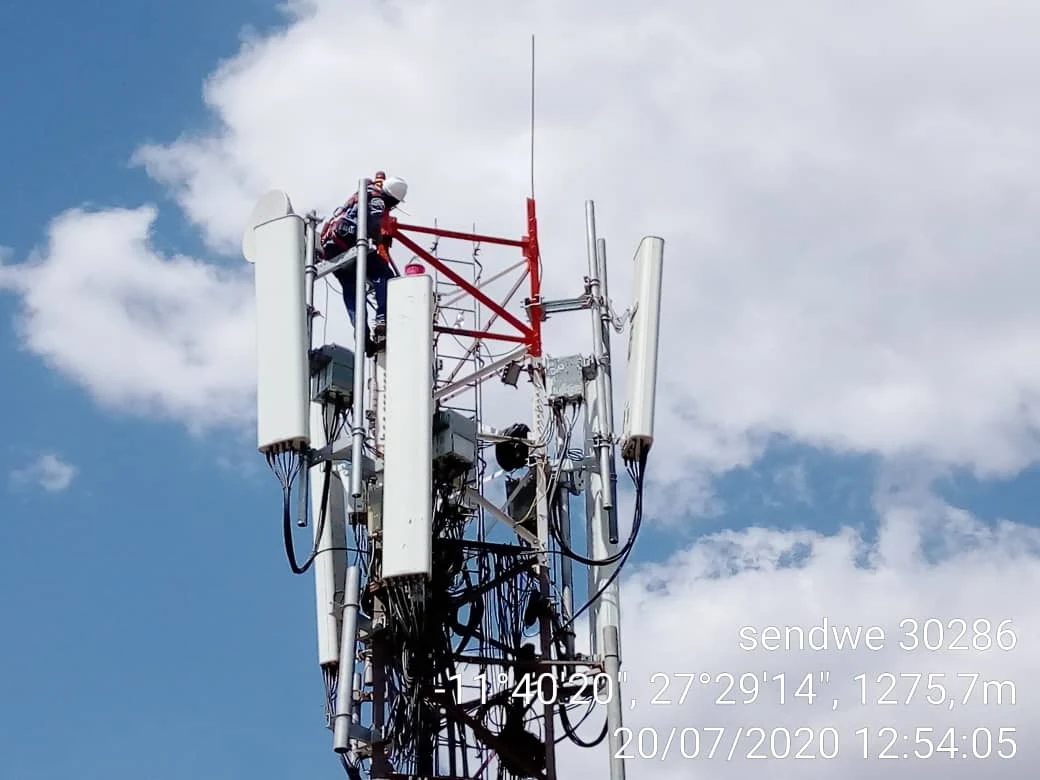 Intervention sur un pylône télécom rouge et blanc, sur fond de ciel bleu
